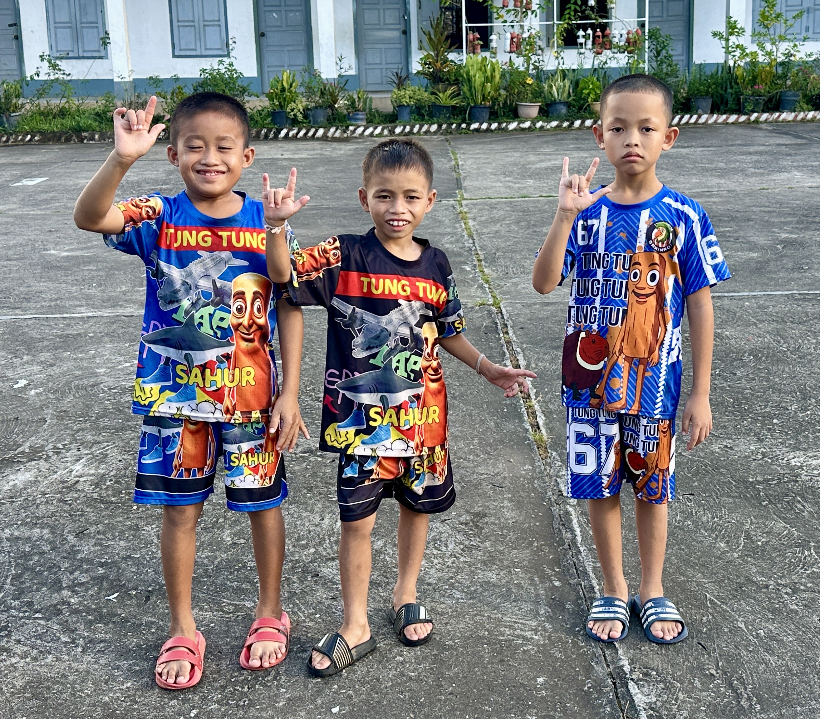 Three students at Luang Prabang School for the Deaf signing hello in the school courtyard