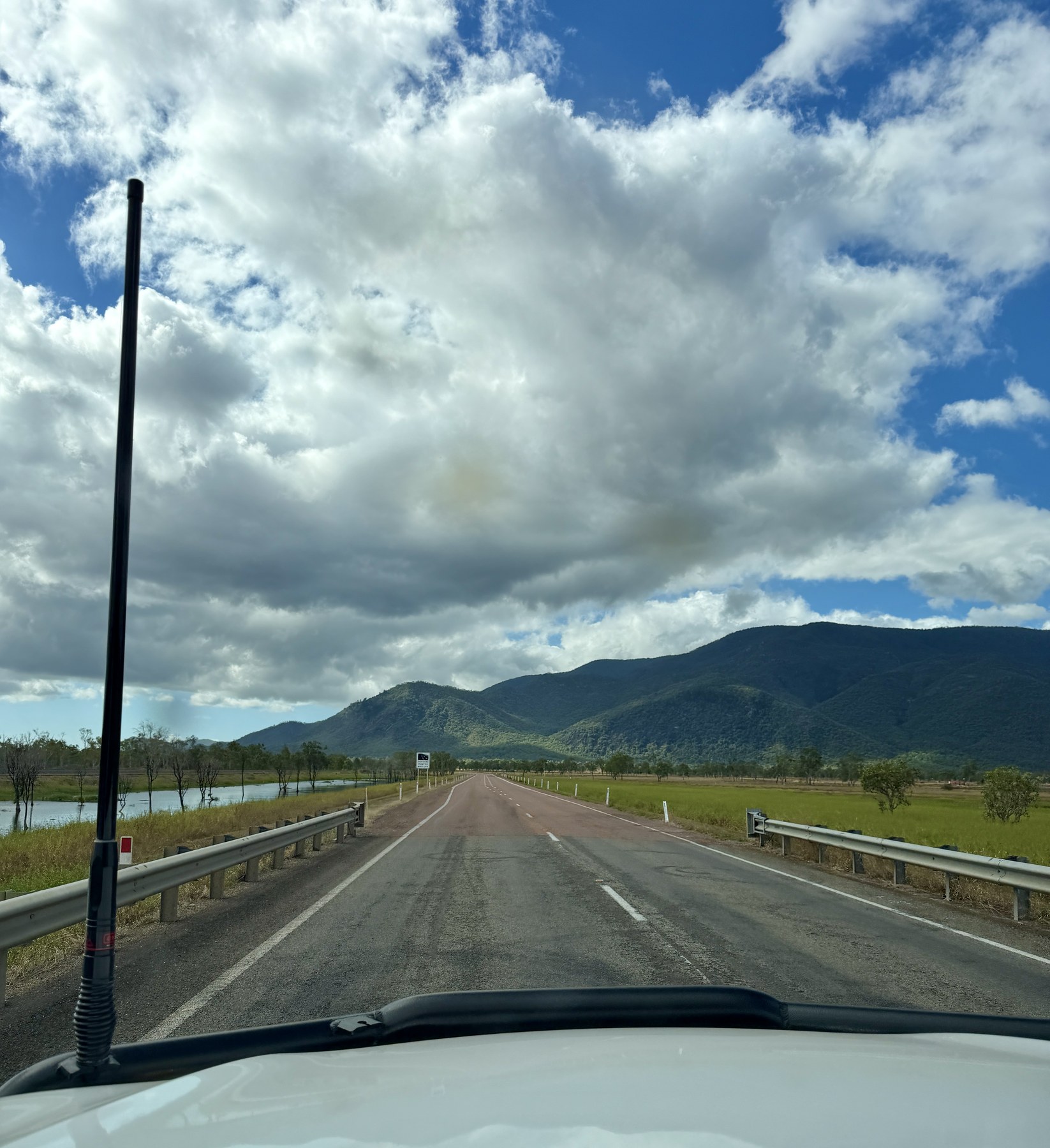 Road stretching ahead towards green hills under large clouds