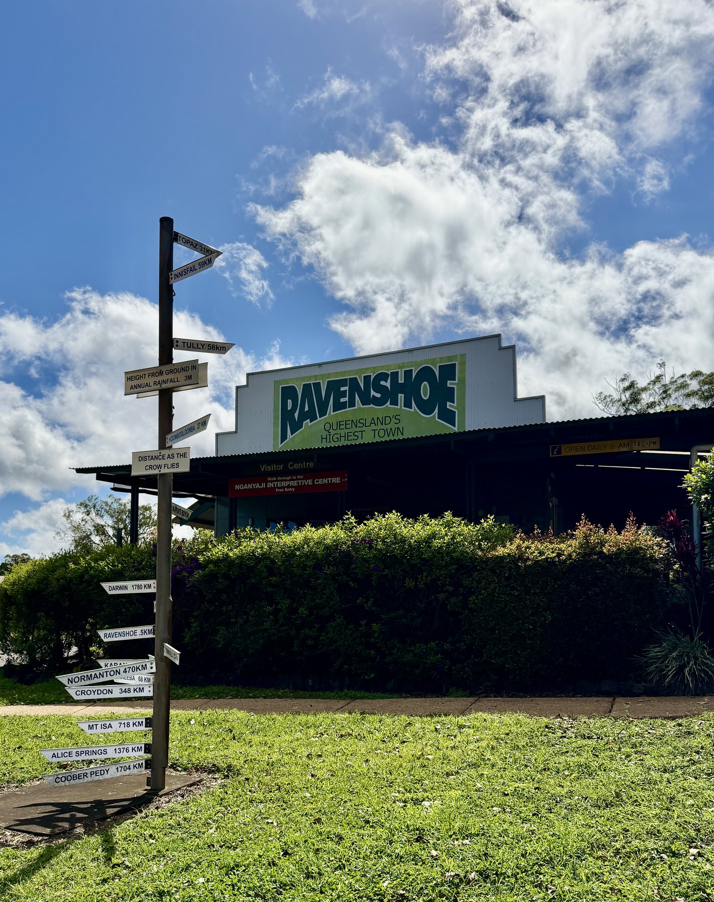 Ravenshoe Visitor Centre sign beside distance markers under a blue sky